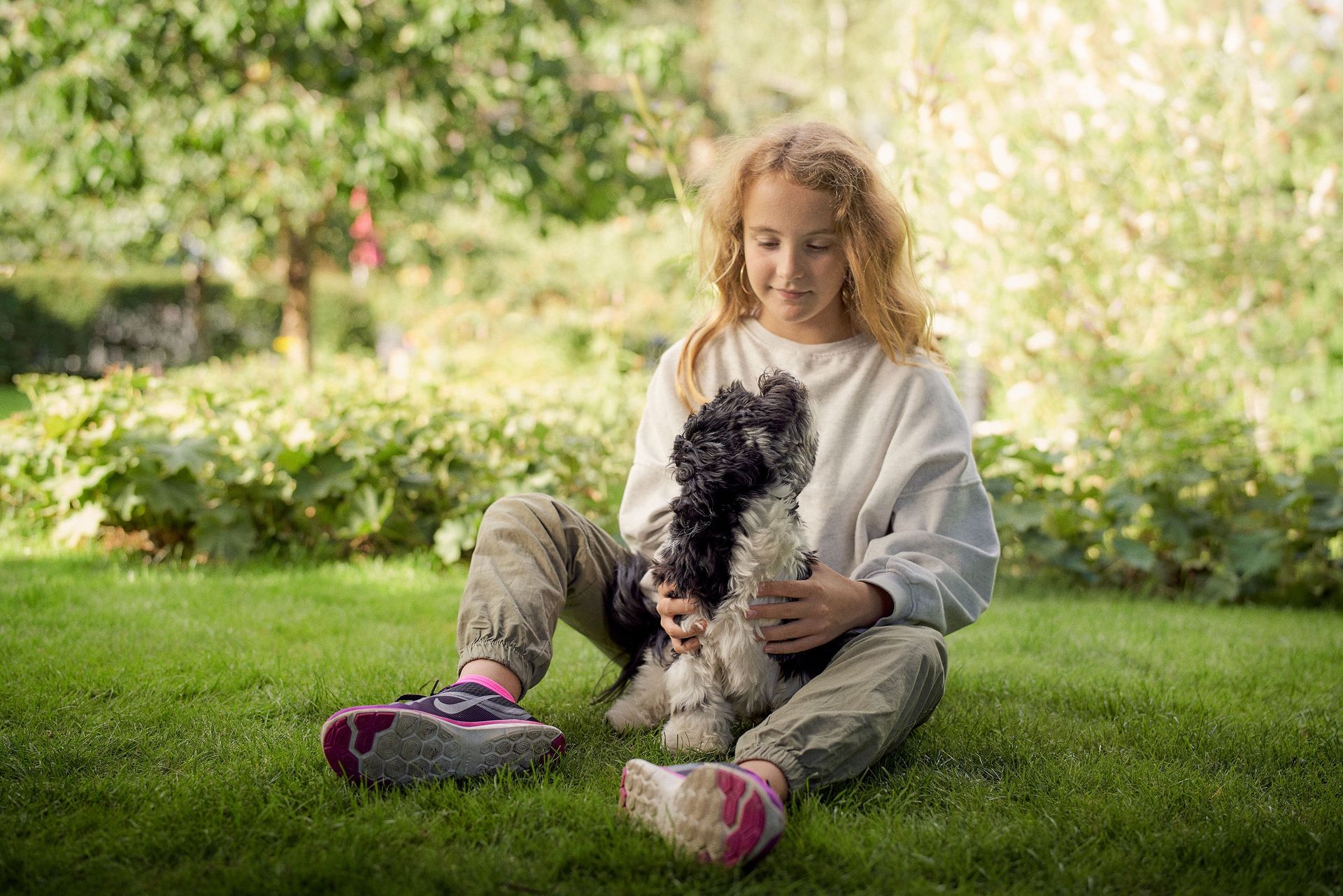 Hund und Mädchen sitzen im Garten und schauen sich an.