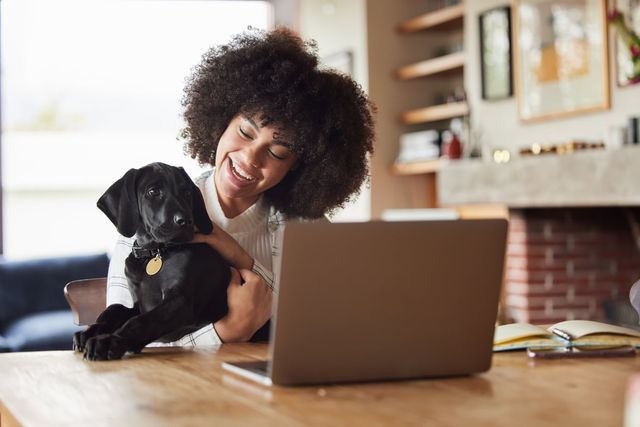 Mädchen, das einen Hund im Arm hält, vor einem Laptop.