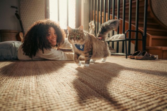 Mädchen liegt auf dem Boden und schaut eine Katze mit einem Agria Katzenspaziergangs-Schal an.